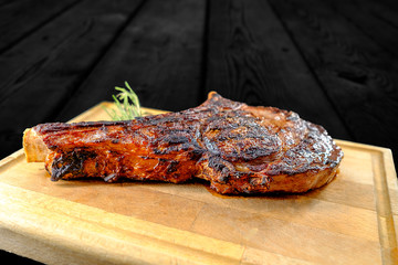 Grilled veal chop on wooden table with spices and herbs. Shot in studio with black wooden background.