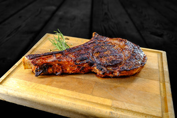 Grilled veal chop on wooden table with spices and herbs. Shot in studio with black wooden background.