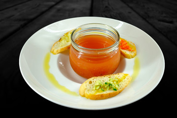 White plate with bowl of vegetarian soup decorated with slices of bread and olive oil.