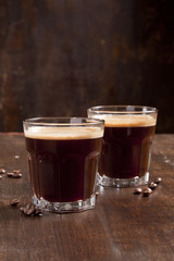 Two americano and coffee beans are on the wooden surface.