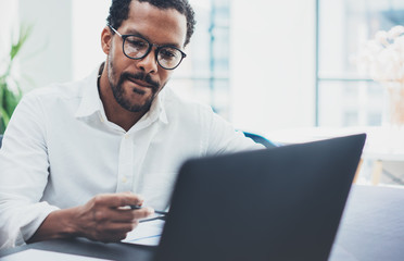 Dark skinned coworker wearing glasses and using laptop in modern office.African american man in...