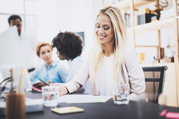 Beautiful Blonde woman working together with colleagues in office. Group of four coworkers discussing business project. Horizontal, blurred background.
