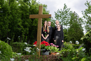 Familie steht in Trauer an Grab auf Friedhof bei Beerdigung