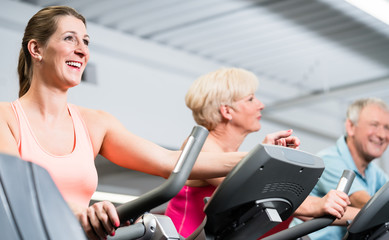 Young woman and senior couple spinning at the gym
