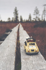 Miniature car is traveling around the world. Caricature car is wondering on a swamp. Duckboards going far away. Image has a vintage effect applied.