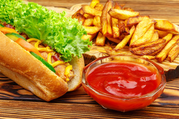 Fast food meal, hot dog, french fries and ketchup on wooden background.