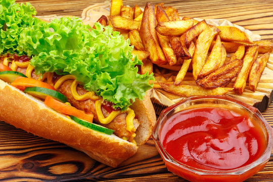 Fast food meal, hot dog, french fries and ketchup on wooden background.