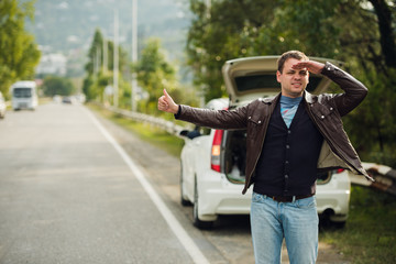 Happy man hitchhiking by a broken car on the road