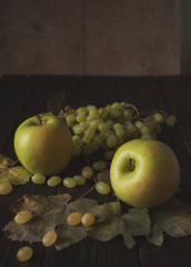 Bunch of grapes, apples and dry leaves on the dark wooden surfac