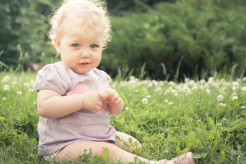 Shy baby girl on grass among blossoming flowers in summer park in sunny day with copy space