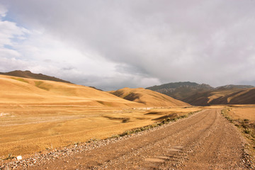 Fototapeta premium Rural road in mountains with overhanging clouds