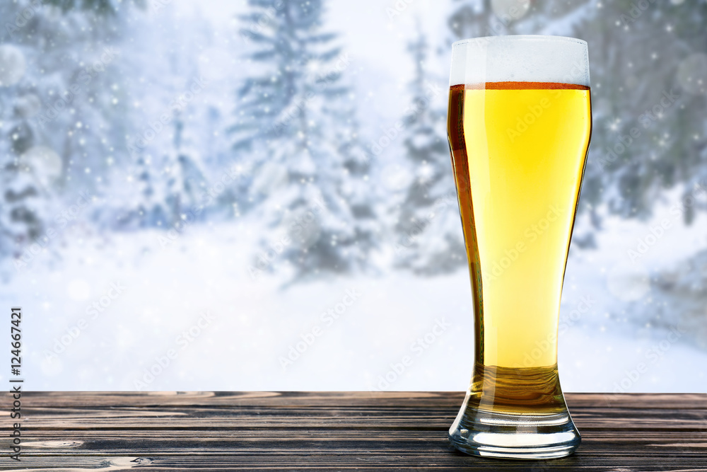 Wall mural glass of beer on wooden table against winter nature background.