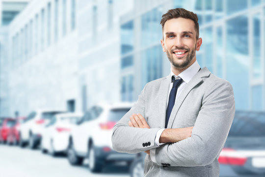 Young businessman on blurred car salon background. Car sale and rent concept.