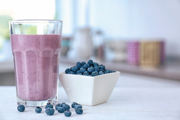 Glass with fresh blueberry smoothie and berries on kitchen table