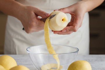 Woman hands peeled apple with knife on wooden table, isolated on