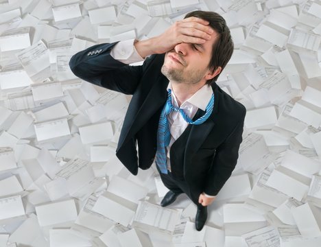 Businessman has headache. Disappointment and failure concept. A lot of bills around.