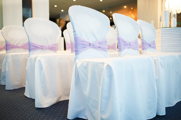 Fototapeta na wymiar White wedding chairs decorated with purple bows