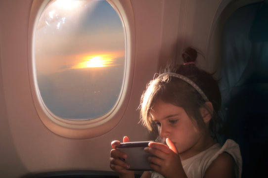 little girl plays with the tablet on the seat of the plane