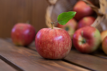 Closeup photo of whole fresh ripe juicy green apple with smooth peel and leaves on shank near basket with burlap on brown wooden table, horizontal photo