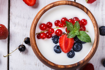 Homemade Yogurt, sour cream in a wooden bowl with different berries,blackberries, strawberries,red currants,raspberries on a white background.selective focus.