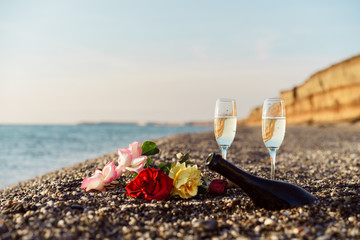 Bottle of champagne, two glasses and rose flowers on the beach. in Greece