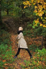 A pretty young blonde woman in a stylish coat and scarf posing on a footpath in autumn forest
