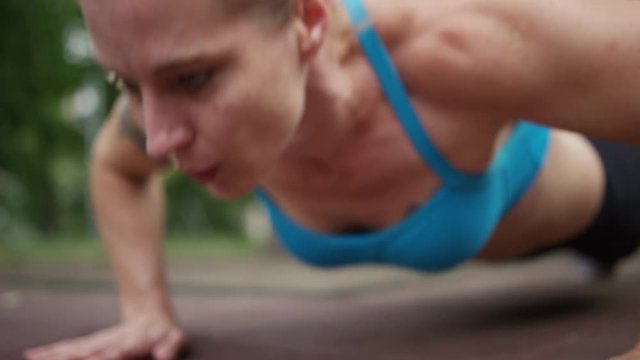 A woman does pushups on the ground outdoors. 4k. In slow motion.
