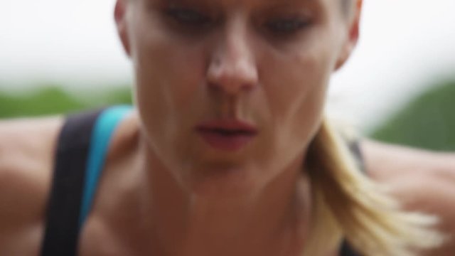 A woman does inclined pushups on bar handles outdoors. Closeup on her face. 4k. In slow motion.