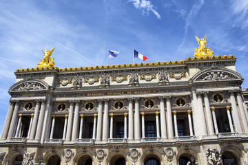 Bottom view of historical, old Paris opera house with clear blue sky background. European and French flags are waving on the top of the building. Golden statues are also in the view.