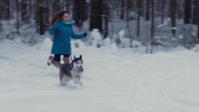 Girl runs with her dog Husky in a winter forest