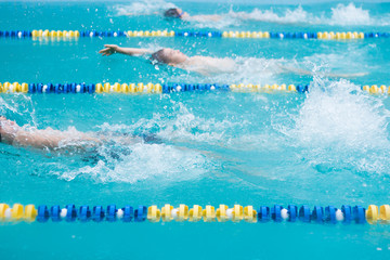 Junior competitive swimming with events in backstroke style. Boys are swimming in a race. Focus on water splash, some motion blur. 