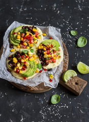 Obraz na płótnie Canvas Spicy bean tostadas with corn salsa and avocado on a rustic cutting board on a dark background. Delicious vegetarian lunch or snack