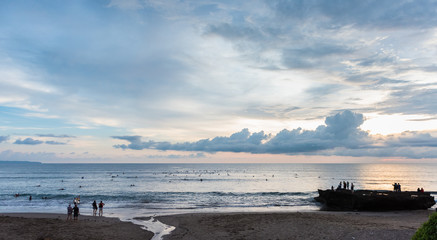 People surfing and watching the sunset at Batu Bolong Beach in Canggu, Bali, Indonesia