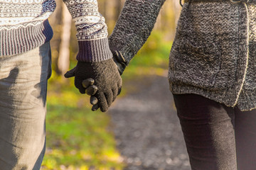Loving couple wearing gloves holding each other by hands and walking in the park on sunset light . Focus point on the man's hand. Close up.