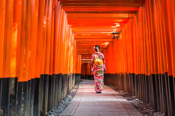 Women in kimono stand at Red Torii gates in Fushimi Inari shrine, one of famous landmarks in Kyoto, Japan