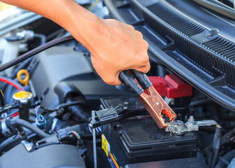 A car mechanic uses battery jumper cables to charge a dead batte