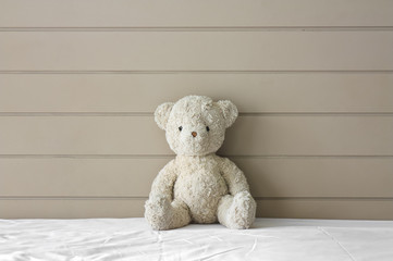 teddy bear sit on the white bed at headboard and brown wall for