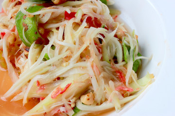 Green Papaya Salad (Som tum Thai) in white dish on wood table, Thai cuisine spicy delicious