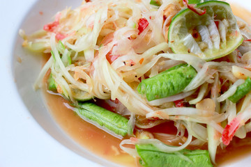 Green Papaya Salad (Som tum Thai) in white dish on wood table, Thai cuisine spicy delicious