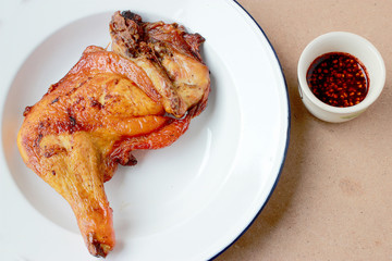 grilled chicken legs in white plate with spicy sauce in small cup  on wooden background. close-up. horizontal view from above.