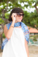 Beauty portrait of sexy brunette woman in white dress on the beach with colorful silk scarf and sunglasses. Cruise summer fashion. Bali, Indonesia.