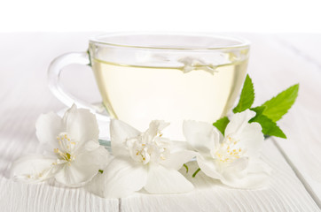 Fototapeta na wymiar Glass cup of tea with jasmine on the white wooden background