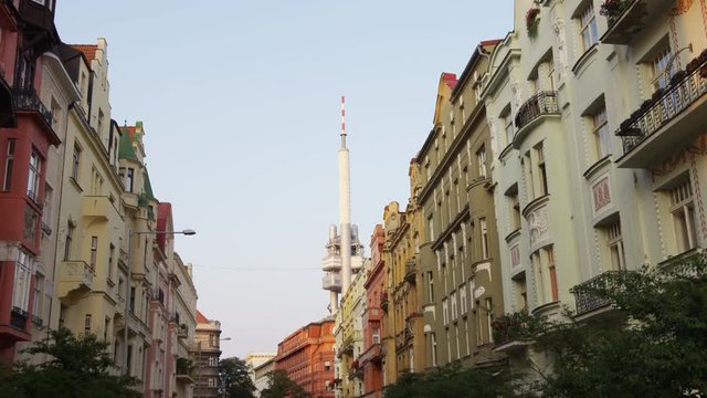 A walking shot down a tree lined Prague street looking up at the building facades with the Zizkov tower in the distance. 4k.
