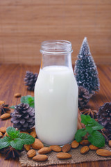 Almond milk in glass bottle with almond nuts on wooden table.