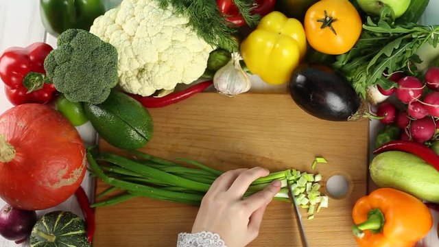Woman cuts green onions among the fresh vegetables