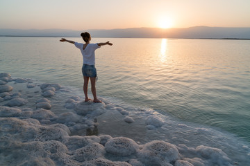 Naklejka premium Girl meets sunrise on the shore the Dead Sea in Israel