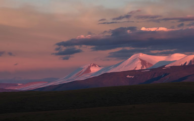 A highland sunset landscape with dramatic colorful illuminated snow ice covered high mountains and glaciers under clouds and blue sunset sky, Plateau Ukok, Altai mountains, Siberia, Russia