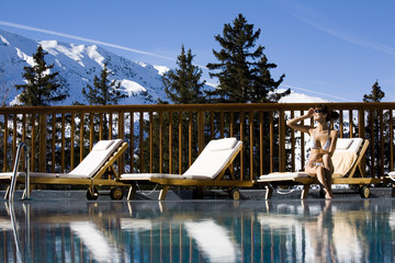 femme souriante assise au bord d'une piscine à la neige dans les montagnes