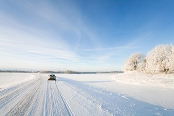 Fototapeta na wymiar Small hatchback car driving along a snowy, icy road on a beautiful, cold and sunny winters day