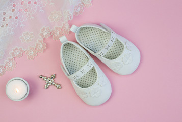 Pair of white baby booties on pink background with vintage lace christening dress